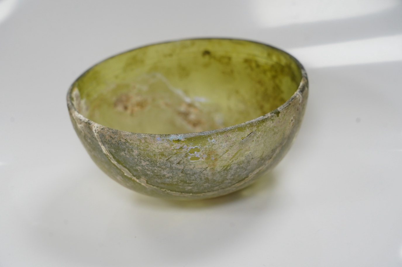 Three items of Roman glassware to include a bowl, a miniature jug and a vessel, bowl 14cm diameter. Condition - bowl repaired